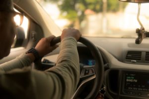 Man driving in car with both hands at top of the wheel.