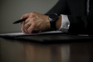 Person in suit resting hands on documents while holding a pen